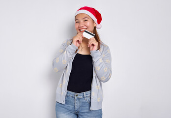 Cheerful and excited young Asian woman in a Christmas hat showing a blank white credit card at camera isolated on white background