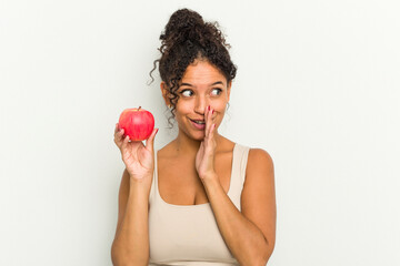 Young brazilian woman holding a red apple isolated is saying a secret hot braking news and looking aside