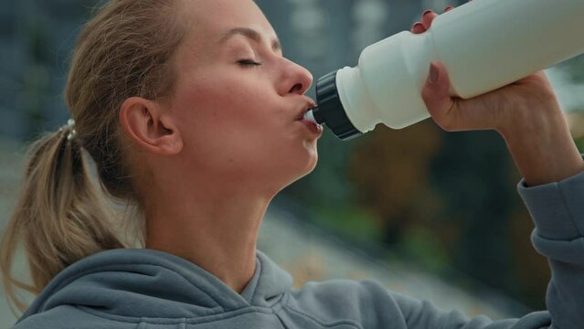 Active healthy caucasian woman athlete girl runner sportswoman tired after sport on city stadium drink cold water energetic beverage hydrate body quench thirst happy female looking at camera feel good