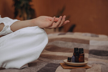 Crop woman with mudra hand doing yoga on bed with essential oils for aromatherapy at home  - obrazy, fototapety, plakaty