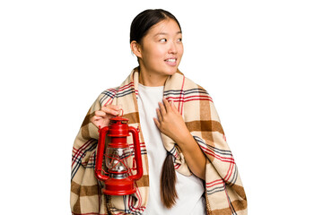 Young asian woman wearing a blanket and holding a lamp isolated looks aside smiling, cheerful and pleasant.