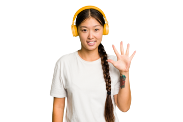 Young asian woman listening to music with headphones isolated smiling cheerful showing number five with fingers.