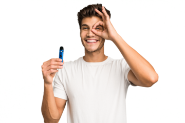 Young caucasian man holding an electronic cigarette isolated excited keeping ok gesture on eye.