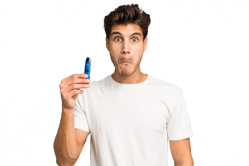 Young caucasian man holding an electronic cigarette isolated shrugs shoulders and open eyes confused.