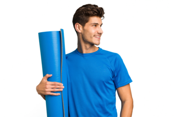 Young caucasian sport man holding a mat isolated looks aside smiling, cheerful and pleasant.