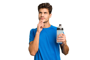 Young sport caucasian man holding a bottle of water isolated looking sideways with doubtful and...