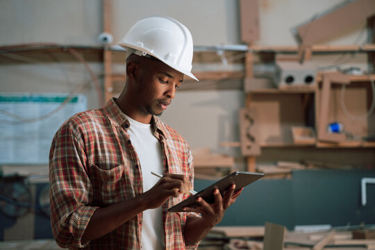 African industrial worker wearing safety hat on digital tablet