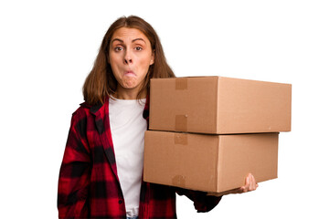 Young caucasian woman moving while picking up a box full of things isolated shrugs shoulders and...
