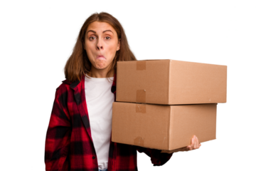 Young caucasian woman moving while picking up a box full of things isolated shrugs shoulders and open eyes confused.