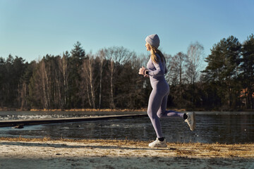 Full length of adult caucasian woman jogging on beach by the lake in the winter