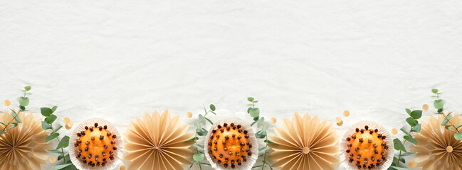 Fototapeta na wymiar Christmas border, copy-space. Fragrant pomander balls handmade from tangerines with cloves. Handmade stars from brown baking paper. Panoramic flat lay on off white textile tablecloth with eucalyptus.