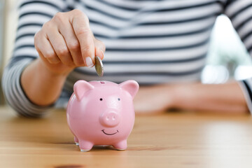 Obraz na płótnie Canvas Woman hand putting money into piggy bank. Concept of money saving and budgeting. Saving money with pink cute piggy bank