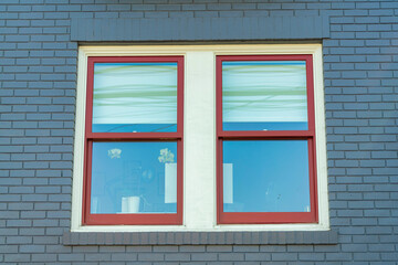 Red framed window with white accents on black or blue brick wall on the side of house or building in shade midday