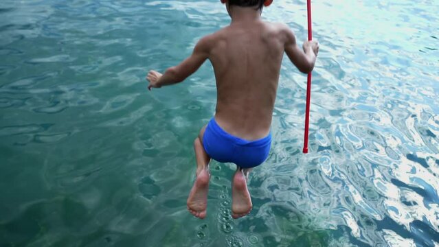 Back of child plunging into water. One small boy jumping into lake in slow motion. Happy kid enjoying summer vacations