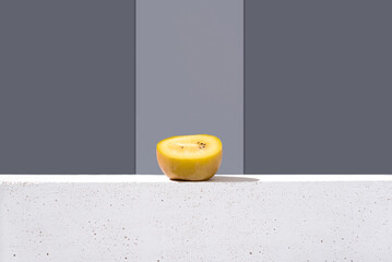 Rebanada de kiwi amarillo dorado sobre un soporte blanco y fondo gris