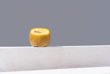 Rebanada de kiwi amarillo dorado sobre un soporte blanco y fondo gris