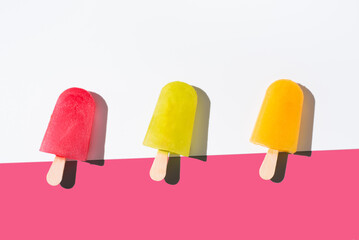 Paletas de hielo de colores. Palitos de helado naranja, rojo y amarillo sobre fondo rosa y blanco. Concepto de verano. Vista superior	