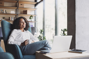 Smiling businesswoman working on laptop computer in office lobby, Young woman professional relaxing...