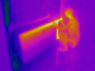 infrared thermal photography of a young woman adjusting the temperature on a room heating radiator