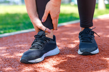 Injury from workout: Young woman use hands hold on her ankle while running on track field..