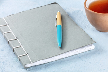 A diary. A paper journal with a pen and a cup of tea on a desk