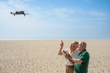 coppia di anziani si diverte con un drone che pilotano in volo in una spiaggia con il cielo blu