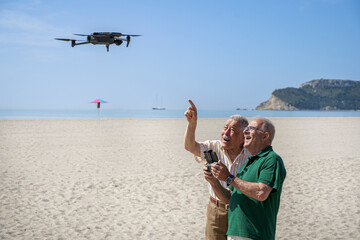 coppia di anziani si diverte con un drone che pilotano in volo in una spiaggia con il cielo blu