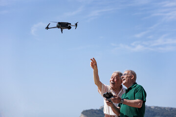 coppia di anziani si diverte con un drone che pilotano in volo in una spiaggia con il cielo blu