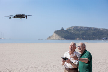 coppia di anziani si diverte con un drone che pilotano in volo in una spiaggia con il cielo blu