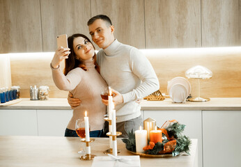 Young happy couple celebrating christmas, holding glasses of wine, hugging, taking selfie
