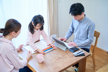 部屋でお絵描きをして遊ぶ母娘と仕事をする父親