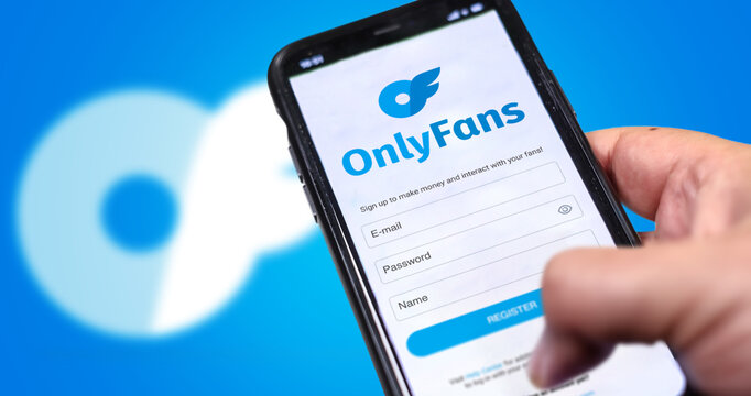 Hand holds a mobile phone with the OnlyFans registration form on the screen and the logo blurred in the background.