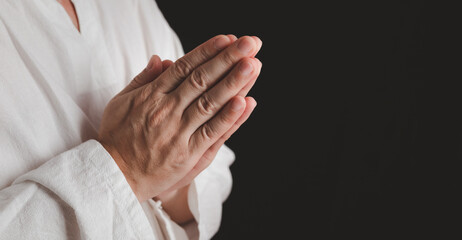An adult whose hand is prayed on the dark background.Respect for belief in religion and God. front view. peace concept.