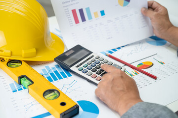 Asian engineer with architectural house plan project blueprint, graph and yellow helmet and...