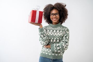 Portrait of young attractive african american woman with curly hair and glasses presenting gift box in studio on white background.