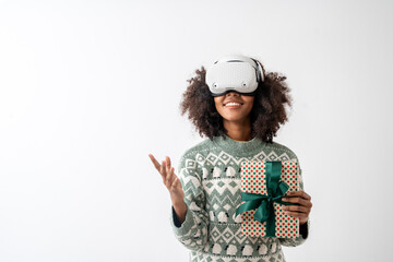 Portrait of young attractive african american woman curly hair with VR goggles holding gift box in studio on white background.
