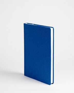  Blue closed notebook in a standing view on a white background. Side view