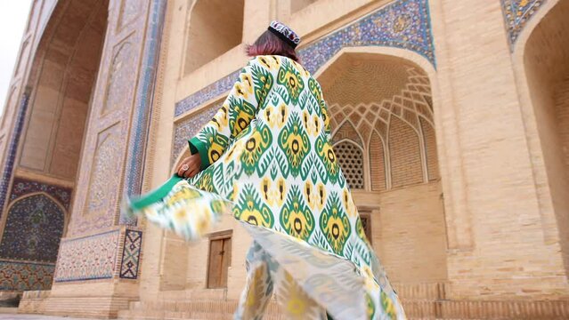 An oriental girl walks in front of an Uzbek Muslim madrasah. Slow motion. National Uzbek women's clothing. Tourist Bukhara.