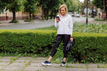 Happy young beautiful woman using her smart phone walking on the city street