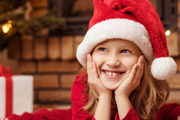 Christmas Smiling Child Portrait Face in Red Santa Hat Close up with Copy Space. Happy Christmas Holidays for Children. 