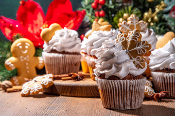 Christmas gingerbread cupcakes. Sweet chocolate and white muffin cupcakes with whipped cream, winter spices and gingerbread cookies decor, on wooden cozy background copy space