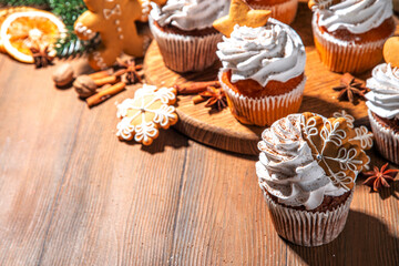 Christmas gingerbread cupcakes. Sweet chocolate and white muffin cupcakes with whipped cream, winter spices and gingerbread cookies decor, on wooden cozy background copy space