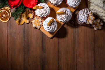 Obraz na płótnie Canvas Christmas gingerbread cupcakes. Sweet chocolate and white muffin cupcakes with whipped cream, winter spices and gingerbread cookies decor, on wooden cozy background copy space
