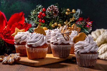 Christmas gingerbread cupcakes. Sweet chocolate and white muffin cupcakes with whipped cream, winter spices and gingerbread cookies decor, on wooden cozy background copy space