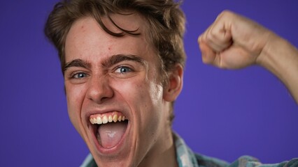 Closeup excited jubilant overjoyed young man 20s doing winner gesture celebrate clenching fist say yes isolated on purple background studio portrait
