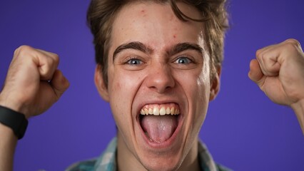 Closeup of excited jubilant overjoyed young man 20s doing winner gesture celebrate clenching fists say yes isolated on purple background studio portrait