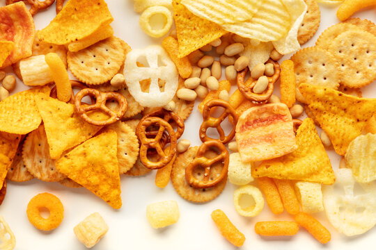 Salty snacks texture on white. Party food assorted mix. Potato and tortilla chips, crackers and other appetizers, shot from the top
