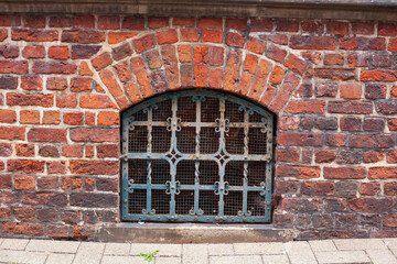 Fototapeta na wymiar Altes Kellerfenster mit Fenstergitter, Rötliche alte Backsteinmauer mit Bogen, Deutschland