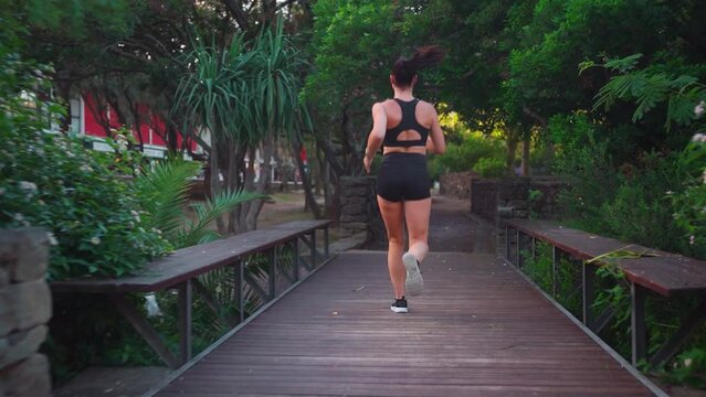 Middle age woman jogging summer day in city park back view. Caucasian female athlete running outdoor. Healthy lifestyle. Morning jogger training. Fit woman jogging outside. Full length follow shoot
