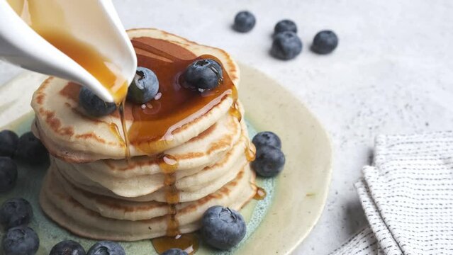 Pancakes with blueberries and maple syrup. The process of cooking breakfast.